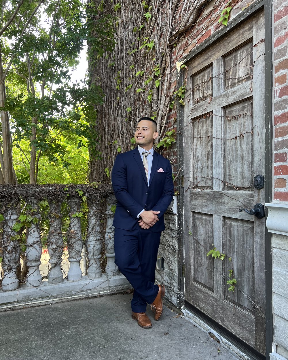 Zhariff Zabidi standing outdoors in a navy suit beside an old wooden door